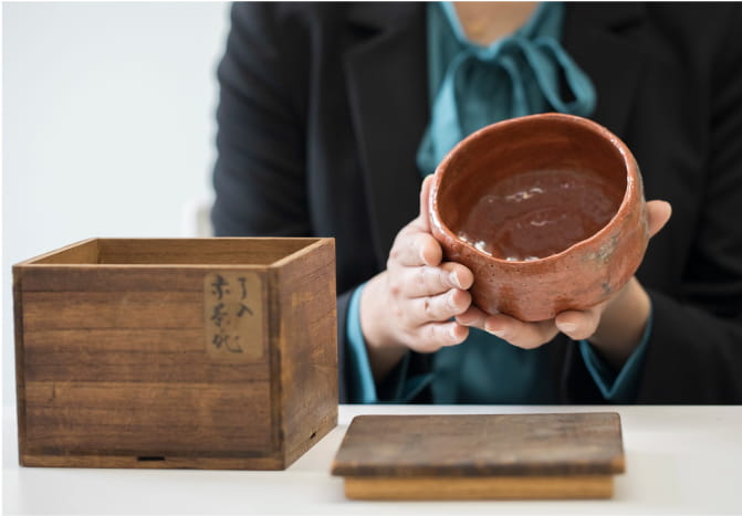 茶碗と木箱を手にする人物